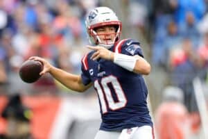 Quarterback throwing football during NFL game, wearing New England Patriots uniform.