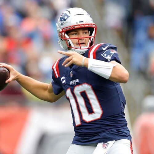 Quarterback throwing football during NFL game, wearing New England Patriots uniform.